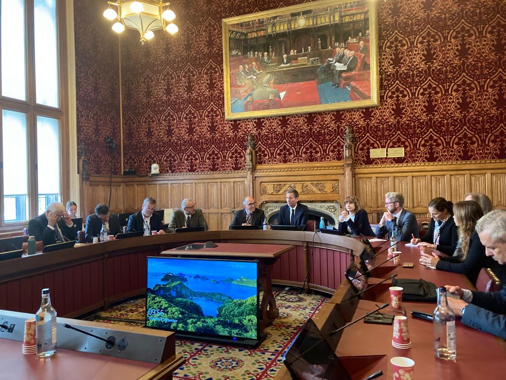 The Electronic Trade Documents Bill Roundtable meeting in House of Lords, Lord Chris Holmes seated at centre and other speakers seated to his left and right at horse shoe shaped table. Ornate red wallpaper and wooden panelling
